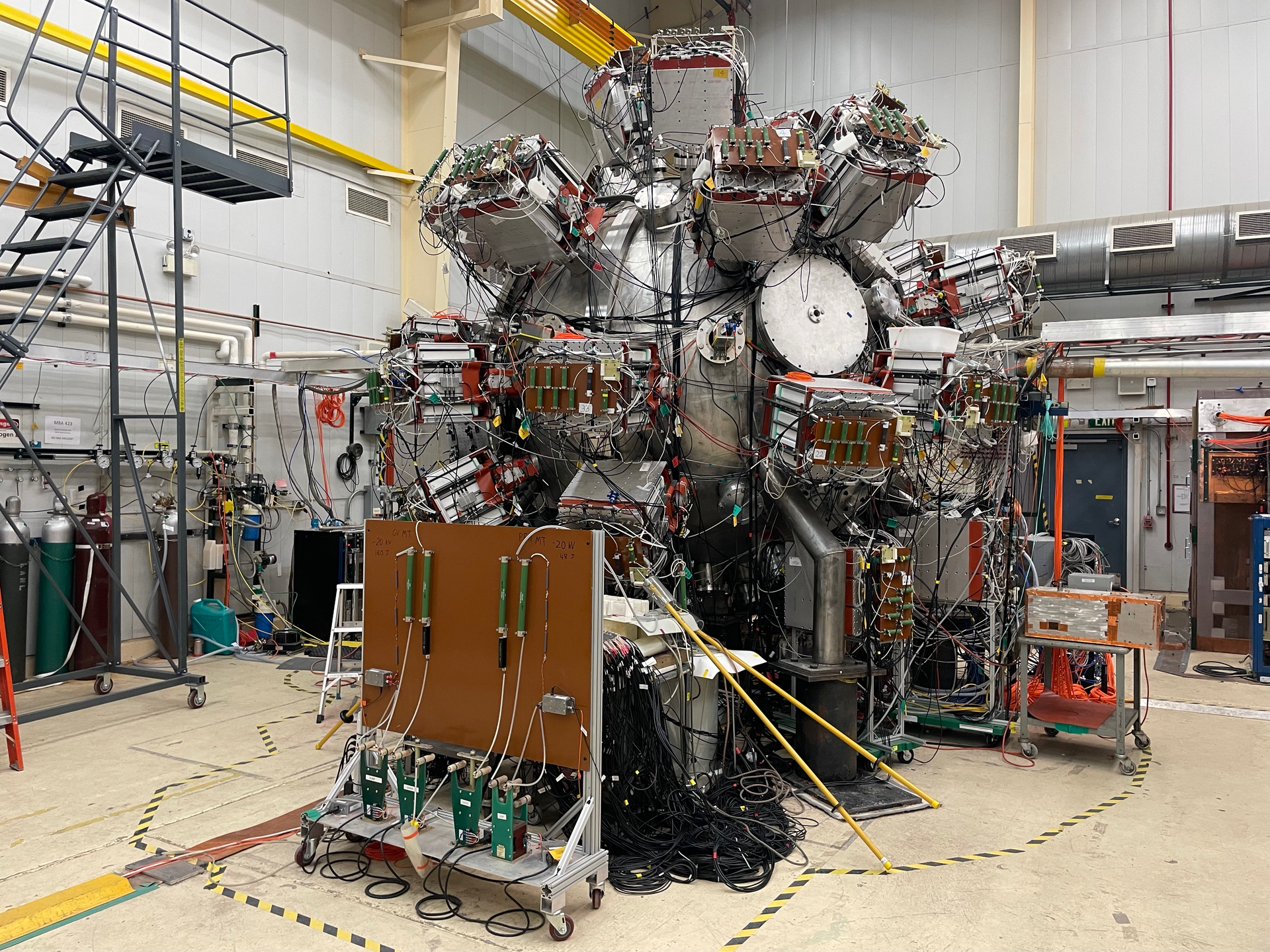 The PLX experiment in a laboratory hall, a spherical steel chamber several meters across with dozens of plasma guns and cabling mounted on its surface.