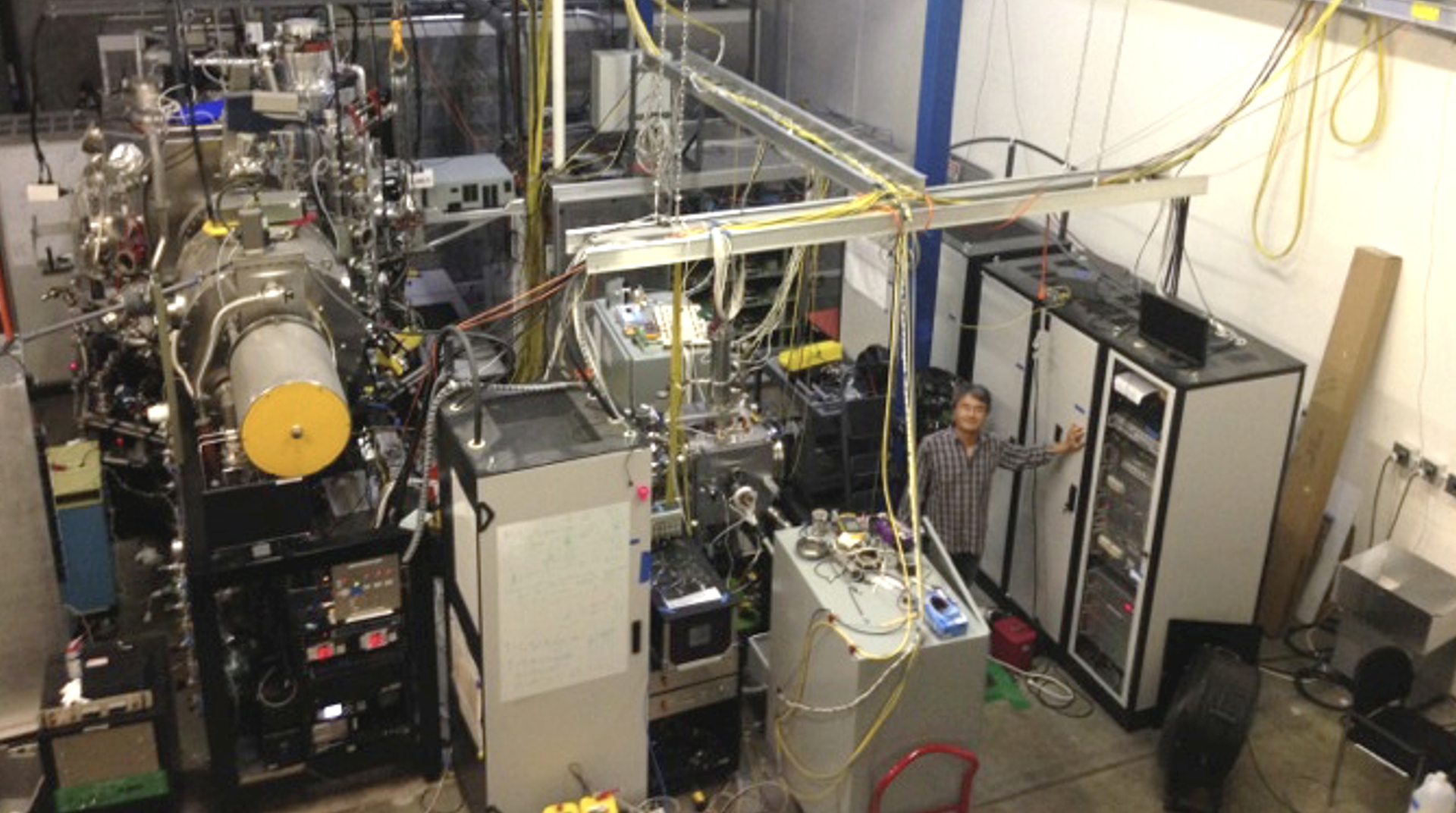 A large experimental setup. Two polywell devices composed of vacuum vessels, diagnostics and pumps. Dr. Park standing next to racks of electronics to the right.